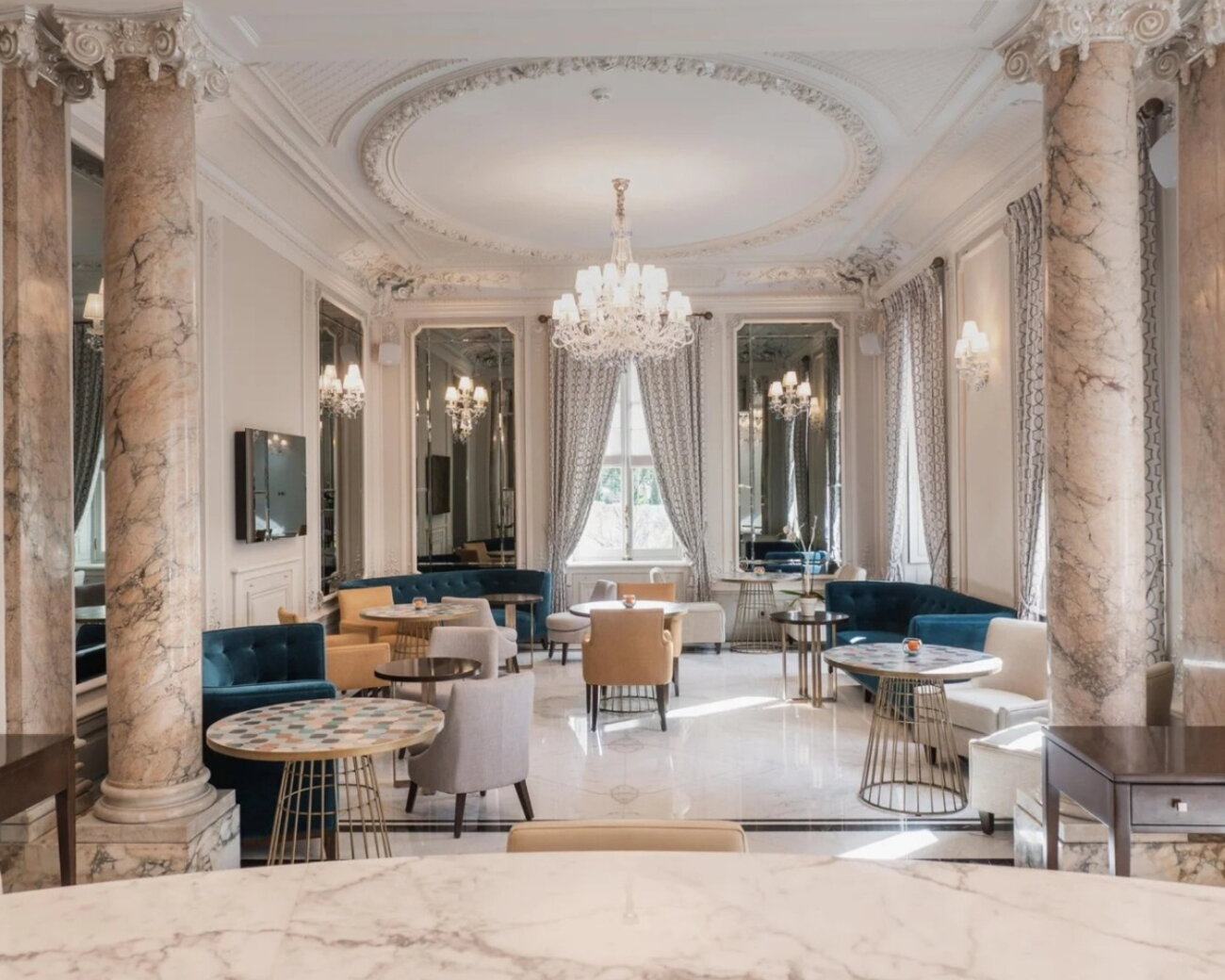 Large crystal chandelier with blue elements reflecting in marble floors and mirrored walls