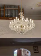 Large crystal chandelier in gold finish hanging in a church with an organ and stucco decoration