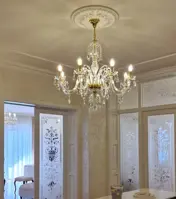 Crystal chandelier with eight arms in gold finish hanging in a luxury interior with etched glass doors
