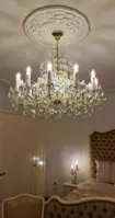 Maria Theresa crystal chandelier in gold finish hanging in a luxury bedroom with upholstered furniture